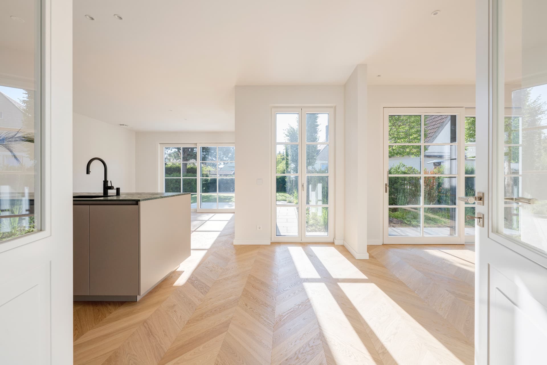 Blick durch die verglaste Doppeltür in den offenen Küchen- und Wohnbereich mit Gartenzugang – Villa Konitzer Straße, München · Bogenhausen