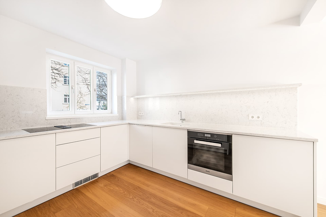 Küche mit weißen Schränken, eingebautem Backofen und Holzboden – Stadthaus Virchowstraße, München · Schwabing