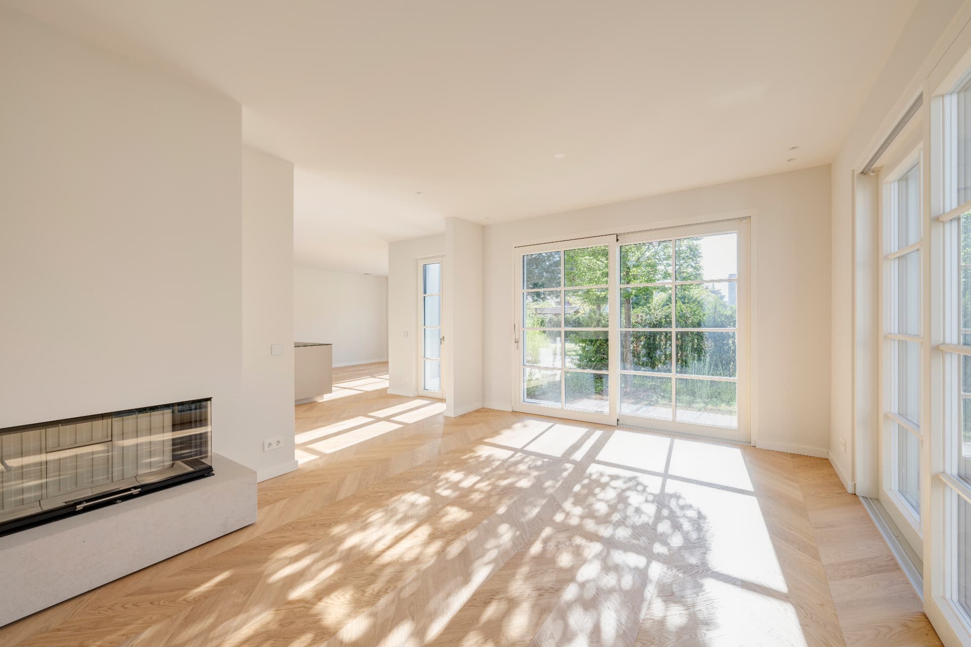 Lichtdurchfluteter Wohnbereich mit Kamin, Holzboden und großen Gartenfenstern – Villa Konitzer Straße, München · Bogenhausen