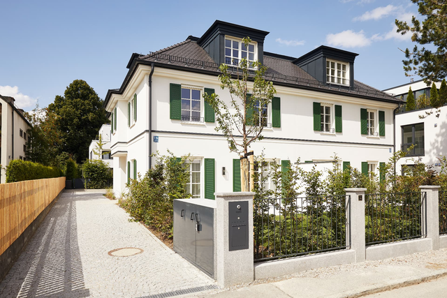 Straßenansicht mit heller Fassade, grünen Fensterläden, Dachgauben und Vorgarten – Villenhälften Dirschauer Straße, München · Bogenhausen